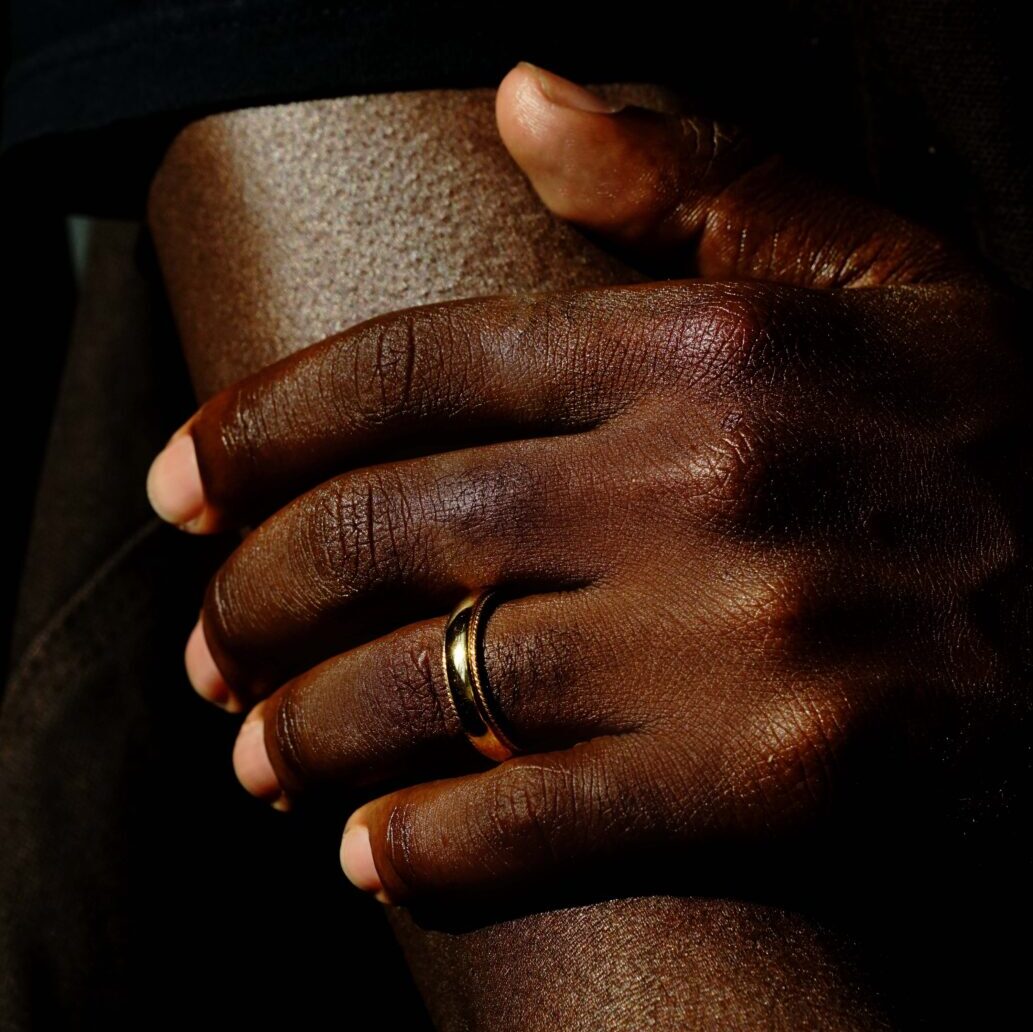 A man wears a wedding band with milgrain details and a polished center