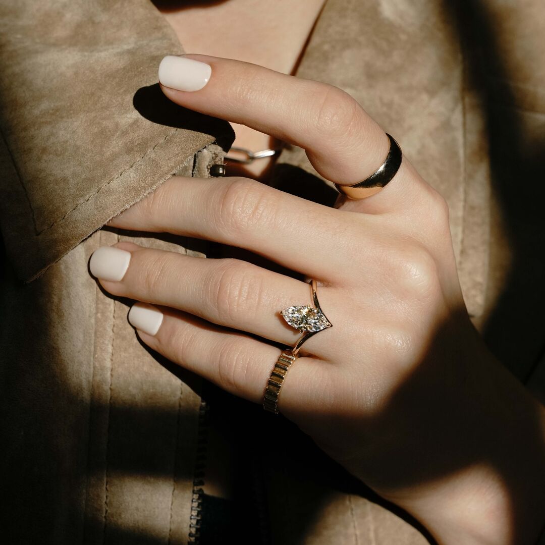 A woman wears an architectural Marquise diamond engagement ring and ribbed yellow gold band 