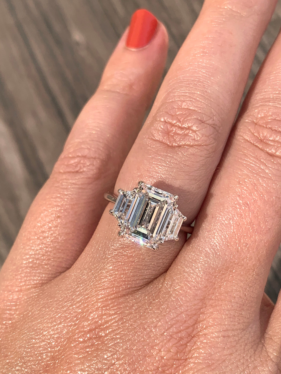 Hand wearing a three stone emerald cut diamond engagement ring set with trapezoid side stones