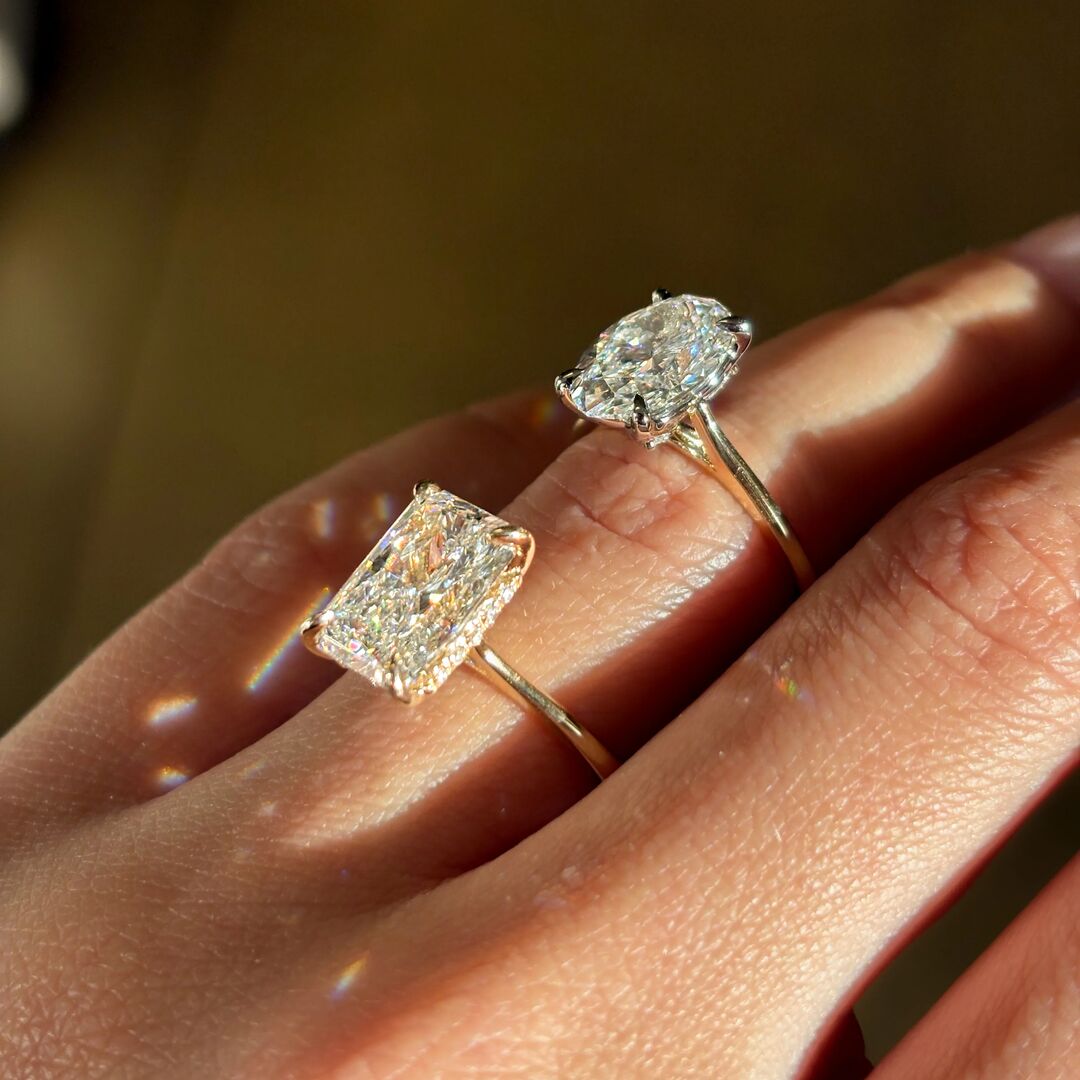 A woman wears two engagement rings. A cathedral, oval solitaire and a hidden halo radiant cut ring. 